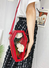 Load image into Gallery viewer, Model holding red vegan leather coffin shaped bag with see through front. Inside of bag has black cross detail. Bag has full zip closure around entirety of coffin shape. Bag has adjustable shoulder strap.